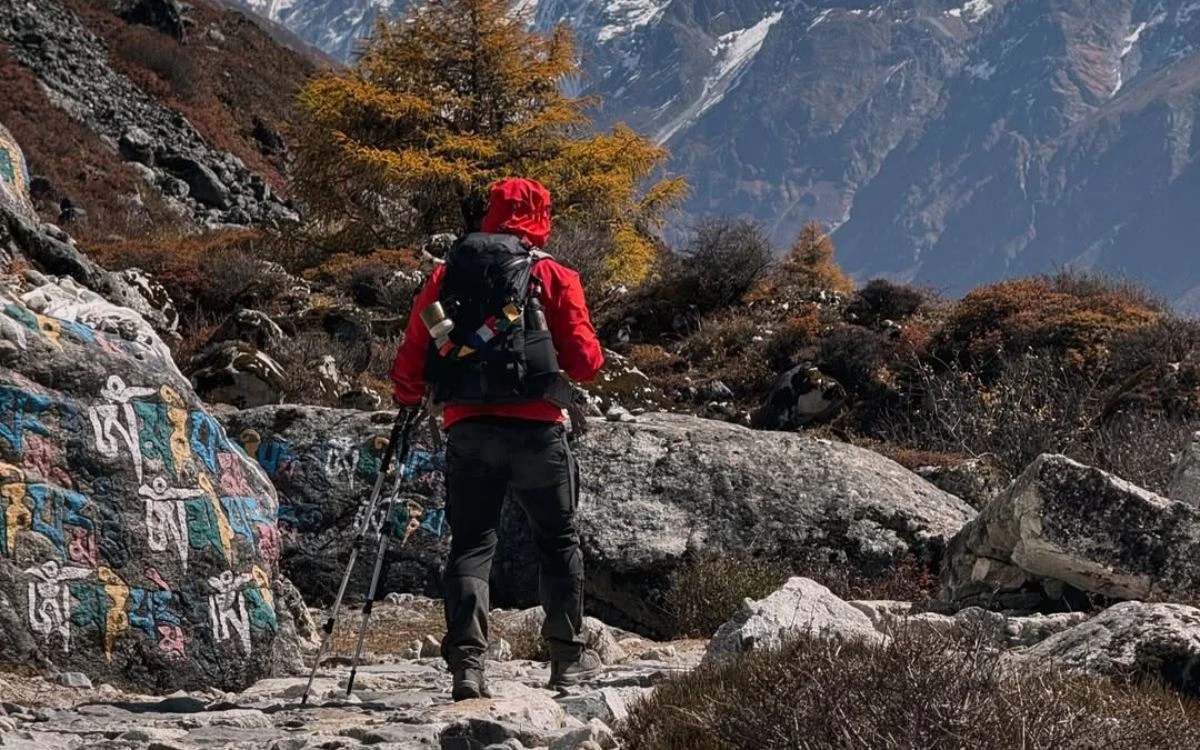 Trekker in red jacket walking past mani stone on Langtang trail