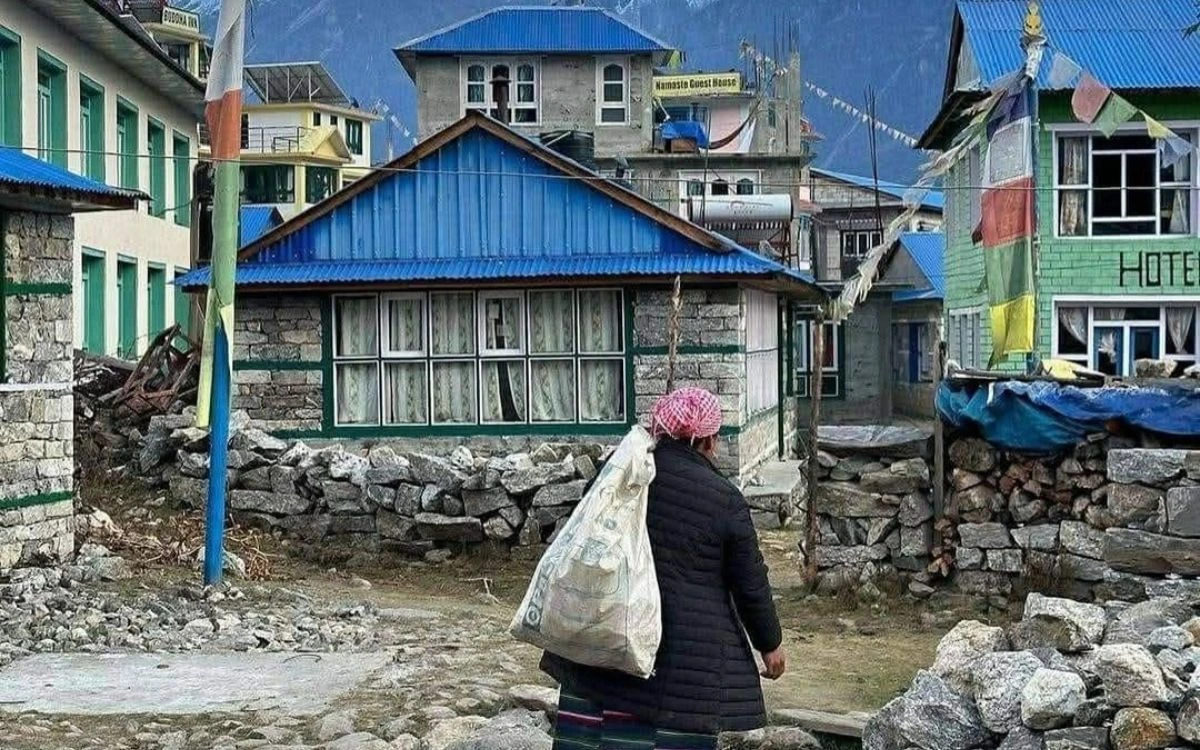Local woman carrying supplies through Langtang village with traditional stone houses