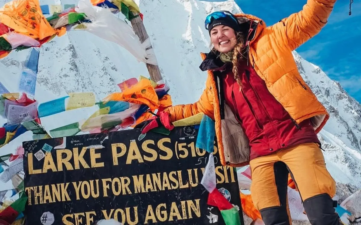 Trekker celebrating at Larke Pass summit (5,106m) with prayer flags and signboard on Manaslu Circuit Trek Nepal