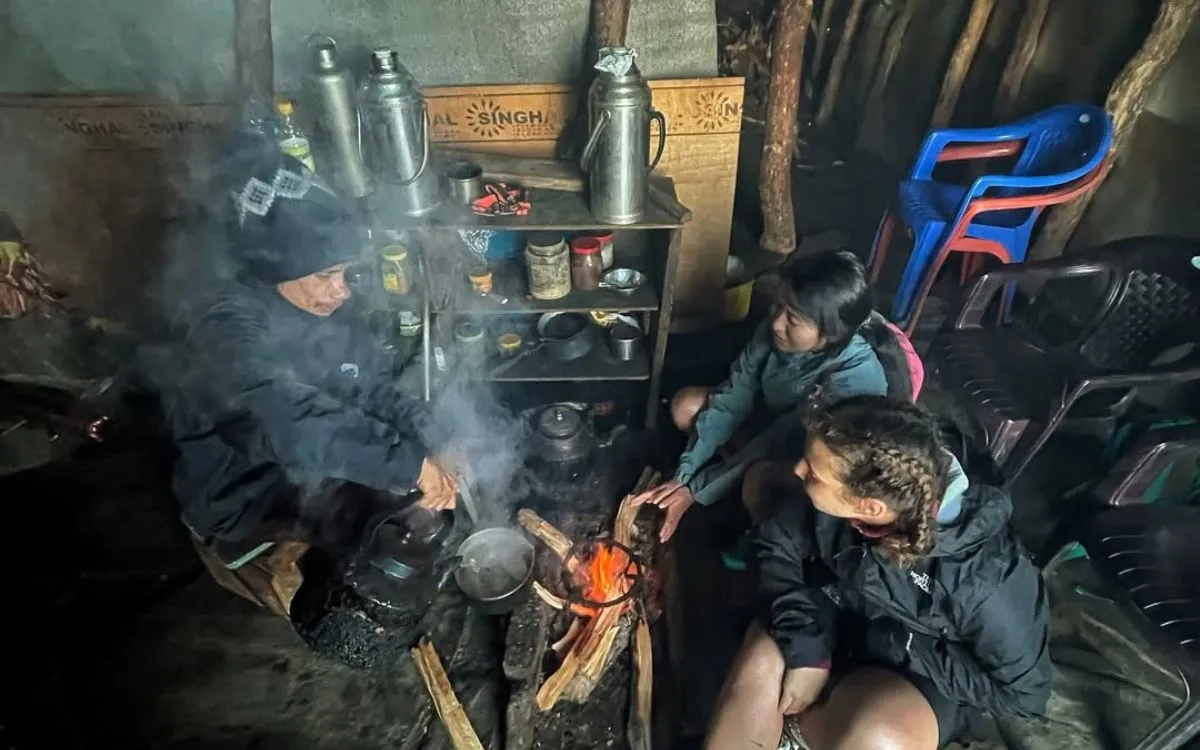 Trekkers warming up by fire inside rustic mountain teahouse at night with basic cooking equipment