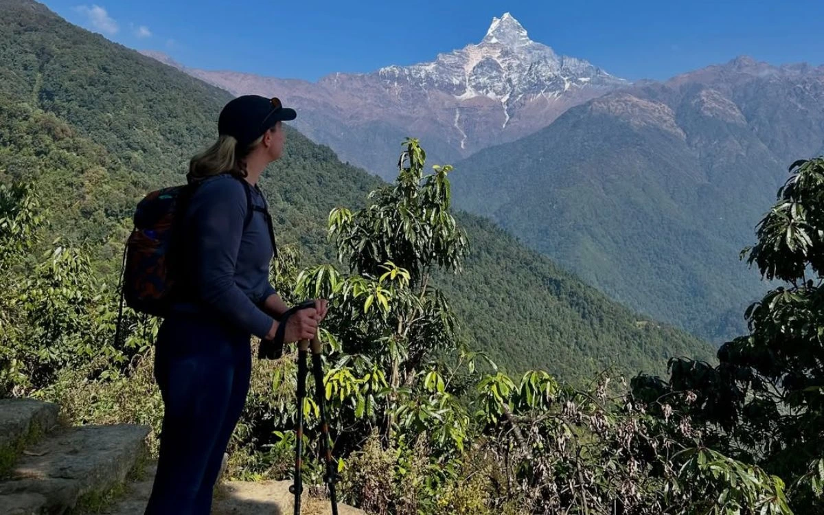 Hiker with backpack and trekking poles looking at snow-capped mountain peak through green valley