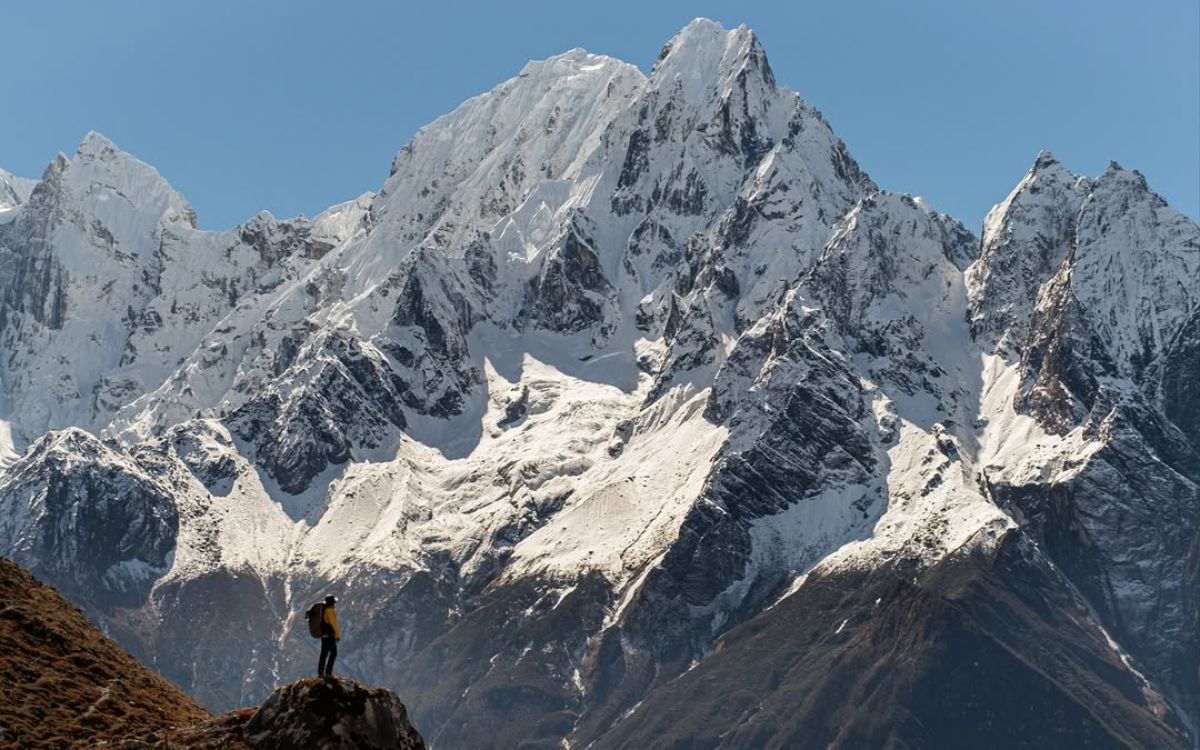 Hiker in yellow jacket viewing Manaslu peak and Himalayan mountain range on Manaslu Circuit trek Nepal