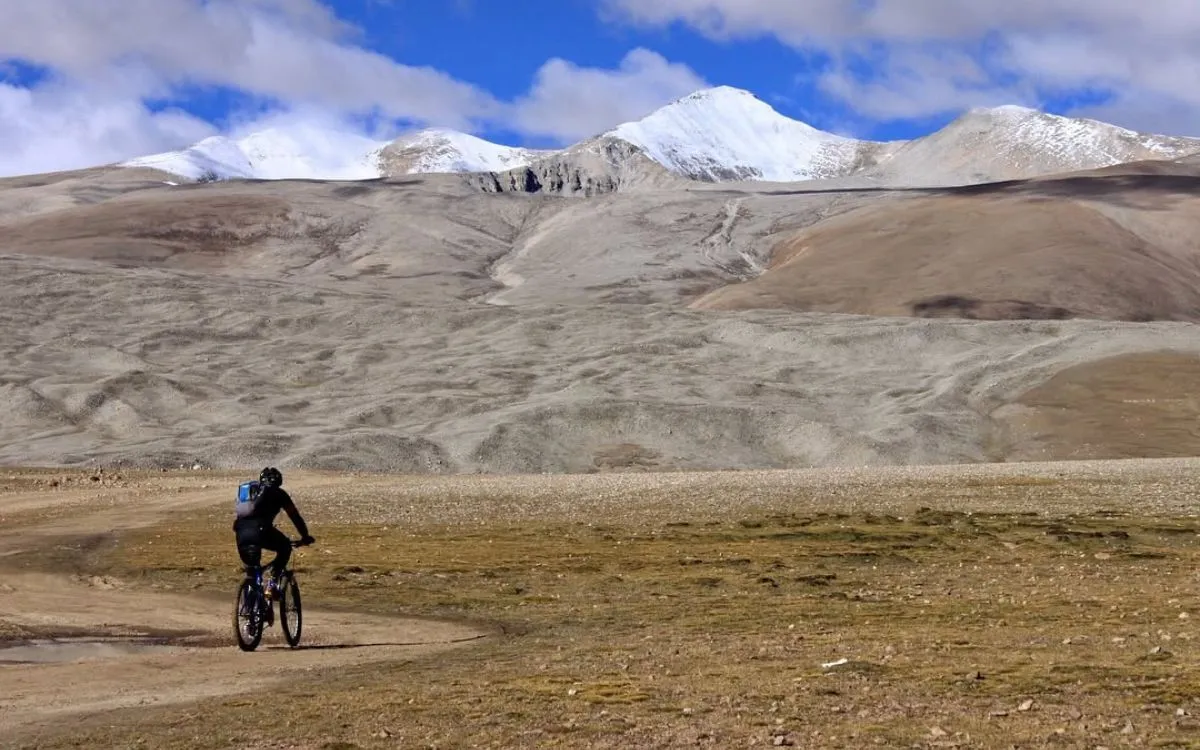 Cyclist riding across barren high-altitude plateau with snow-capped mountains in background