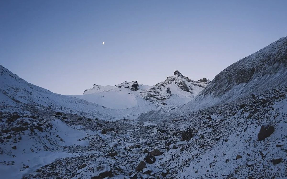 Pre-dawn view of the snow-covered Thorong La Pass approach with the moon in a twilight sky
