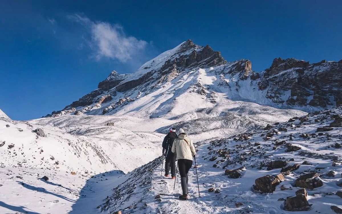Two trekkers with poles ascending the steep snowy trail toward Thorong La Pass at 5,416m