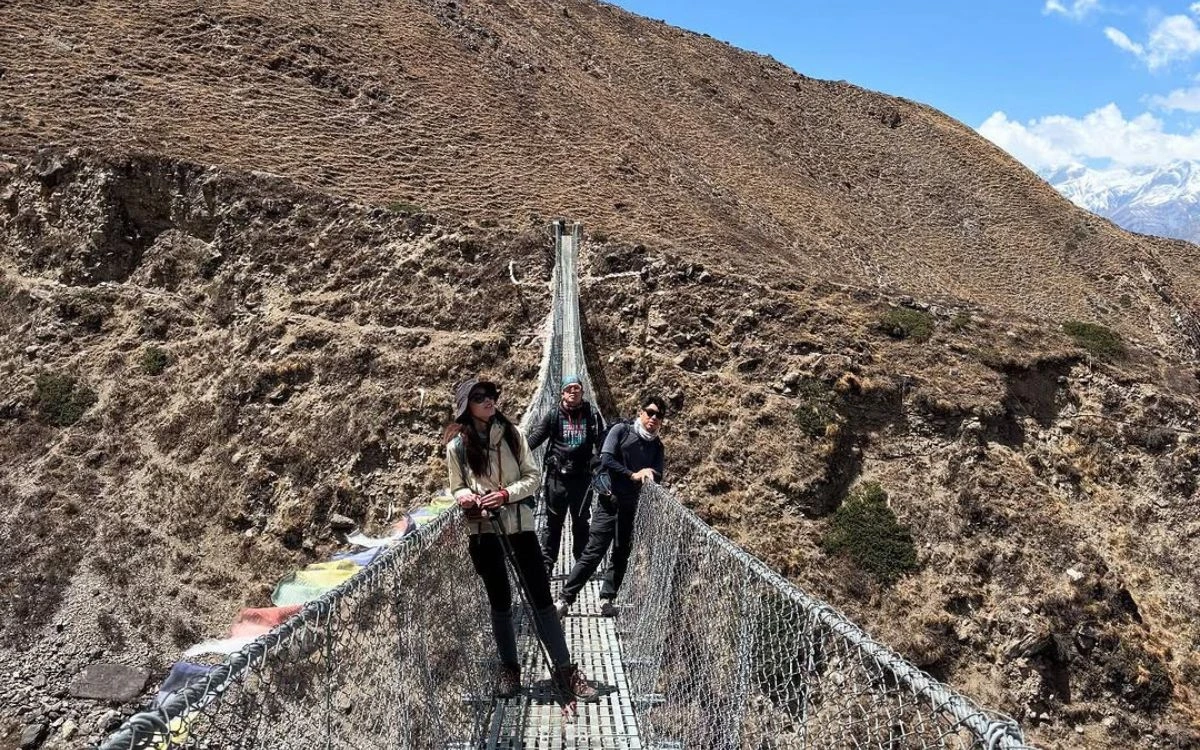 Three trekkers crossing a suspension bridge on the Annapurna Circuit trail toward Thorong La Pass